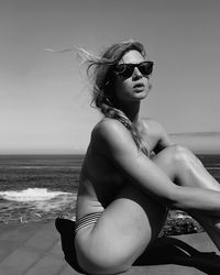 Young woman wearing sunglasses sitting on sea against sky