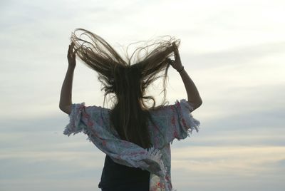 Woman with tousled hair standing against cloudy sky