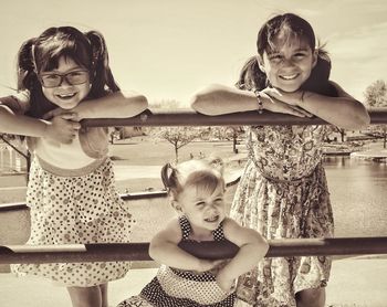 Siblings leaning on railing against sky