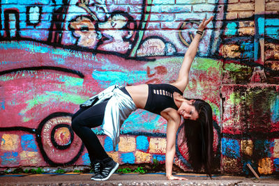 Full length of young woman standing against graffiti wall