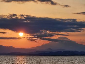 Scenic view of mount fuji against the sea at sunset with scattering clouds