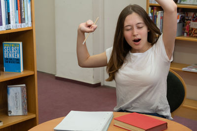 Young woman yawning while sitting at table in library