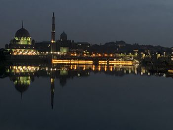 Illuminated buildings by lake against sky at night