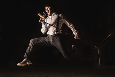 Full length of man singing while holding microphone over black background