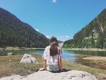 Rear view of woman sitting on mountain against sky