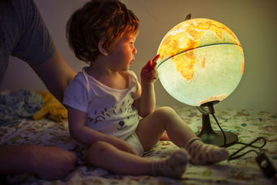 Cute boy in bed looking at a globe of the world 