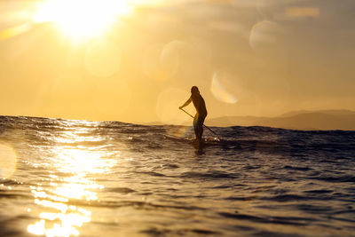 Silhouette man standing in sea against sky during sunset