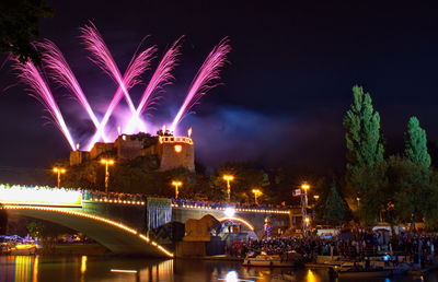 Firework display over illuminated city against sky at night