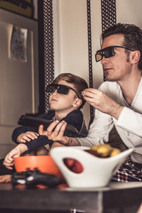 Father and son wearing 3d glasses while sitting on sofa