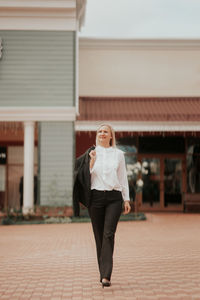 A confident smiling businesswoman in a white shirt and business suit walking along the street