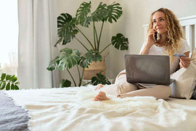 Smiling woman talking on phone while sitting on bed at home