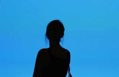 Rear view of silhouette woman standing against clear blue sky