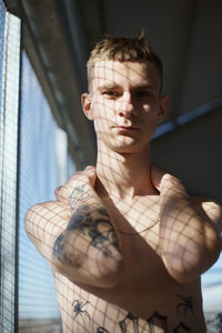 Portrait of shirtless man with tattoo standing against wall