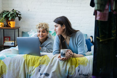 Female friends looking at laptop while relaxing on bed at home