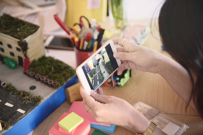 Cropped image of female engineer photographing architectural model through mobile phone at table in office