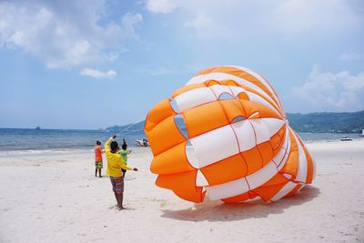 Man with parachute standing at beach against sky