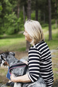 Side view of happy senior woman sitting with dog at field