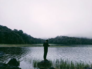 Rear view of man standing in lake with cloudy weather in the morning