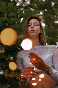 Young woman standing against illuminated tree