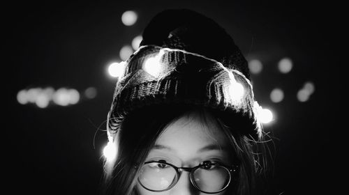 Close-up portrait of girl wearing eyeglasses with illuminated string lights