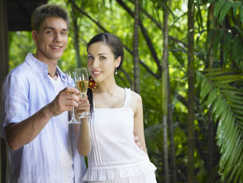 Portrait of smiling young couple with drink standing against plants