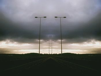 Road passing through field against cloudy sky