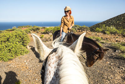 Woman riding horse against sea on field during sunny day