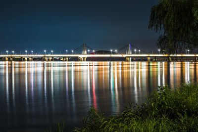 Illuminated bridge over river against sky at night