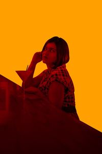 Portrait of young woman looking away against orange sky