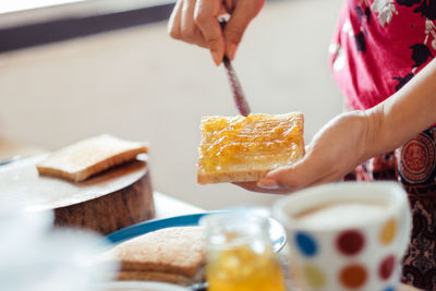 Cropped image of woman spreading orange jam on bread at home