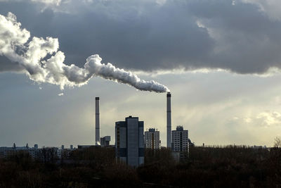 Distant factory emitting smoke against cloudy sky