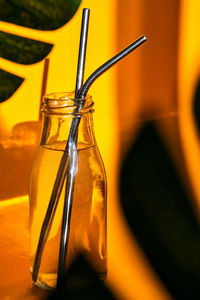 Reusable metal straws in glass bottle with water on yellow background with plant shadow - stainless 