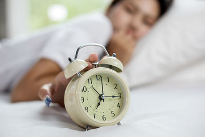 Young woman touching alarm clock while lying on bed at home