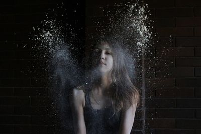 Portrait of teenage girl amidst powder in mid-air against brick wall