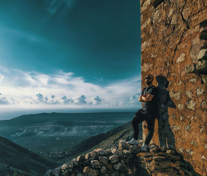 Man standing on rock by sea against sky