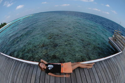 Fish-eye lens view of woman relaxing by sea against sky