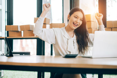 Portrait of smiling young woman using phone while sitting on table