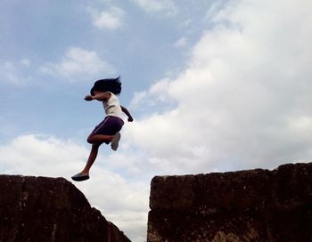 LOW ANGLE VIEW OF YOUNG MAN JUMPING AGAINST CLOUDY SKY
