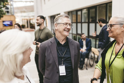 Happy senior businessman talking with female entrepreneurs at networking event in convention center