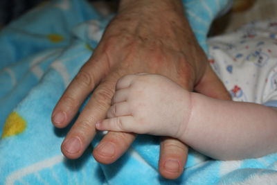 Cropped image of parent and baby holding hands at home