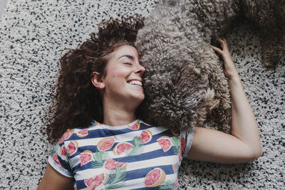 Smiling woman with dog lying on carpet at home