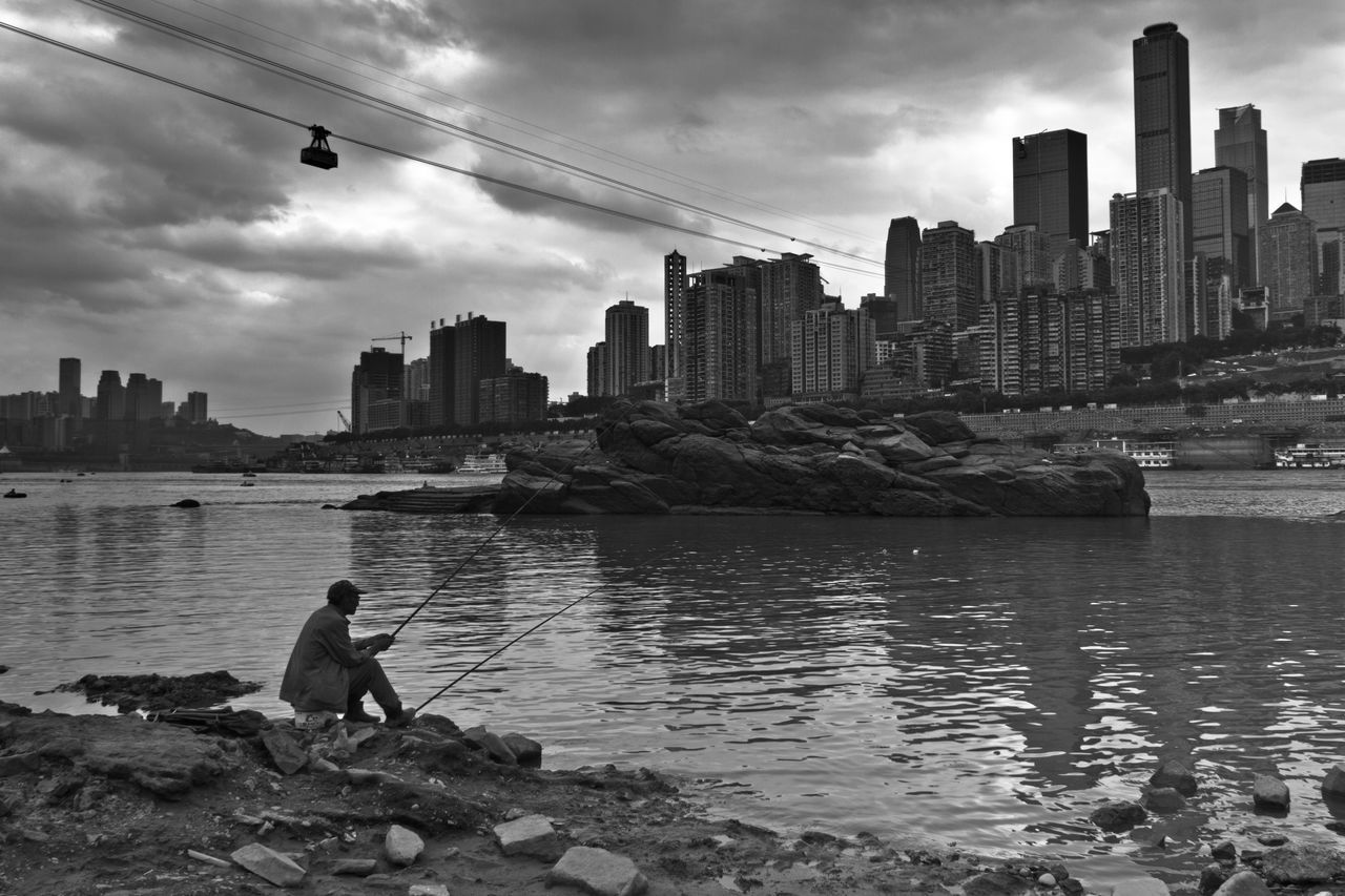 water, sky, men, lifestyles, building exterior, built structure, architecture, leisure activity, city, cloud - sky, river, rear view, person, nautical vessel, transportation, standing, cloud, sitting