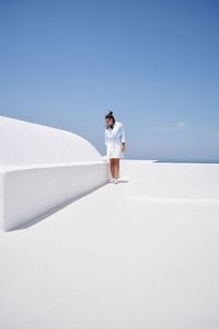 Woman standing on white footpath against clear blue sky