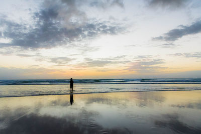 Silhouette person standing on beach against sky during sunset