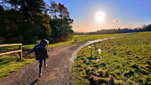 Rear view of woman walking on field against sky