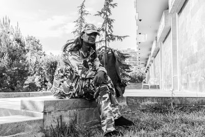 Portrait of young man in camouflage clothing sitting on retaining wall
