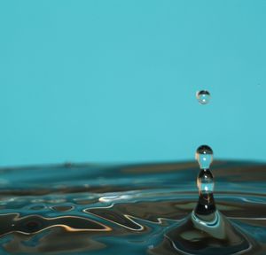 Close-up of drop splashing on water against blue background