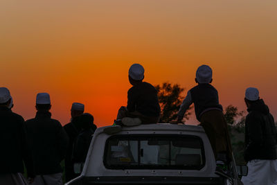 Rear view of people standing against orange sky