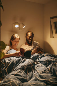 Man and woman reading books while resting on bed with blanket at home