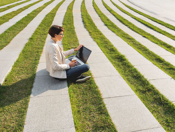 Business woman sits in park with laptop and take away cup of coffee. urban lifestyle of millennials.